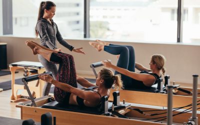 Women doing pilates exercises lying on pilates workout machines while their trainer guides them. Two fitness women being trained by a pilates instructor.